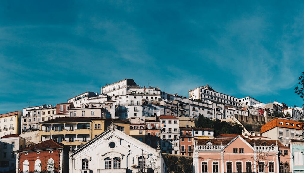 Picturesque cityscape of Coimbra, Portugal showcasing colorful hillside architecture under a bright blue sky.
